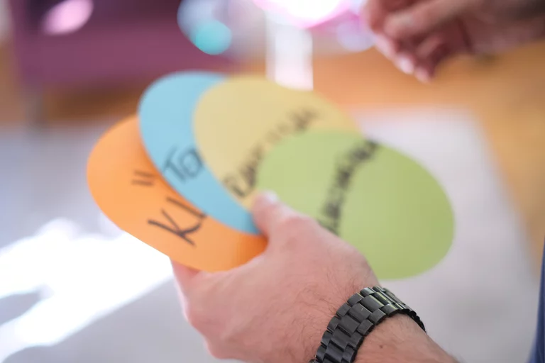 Sebastians Hand hält vier runde Moderationskarten mit Begriffen darauf.